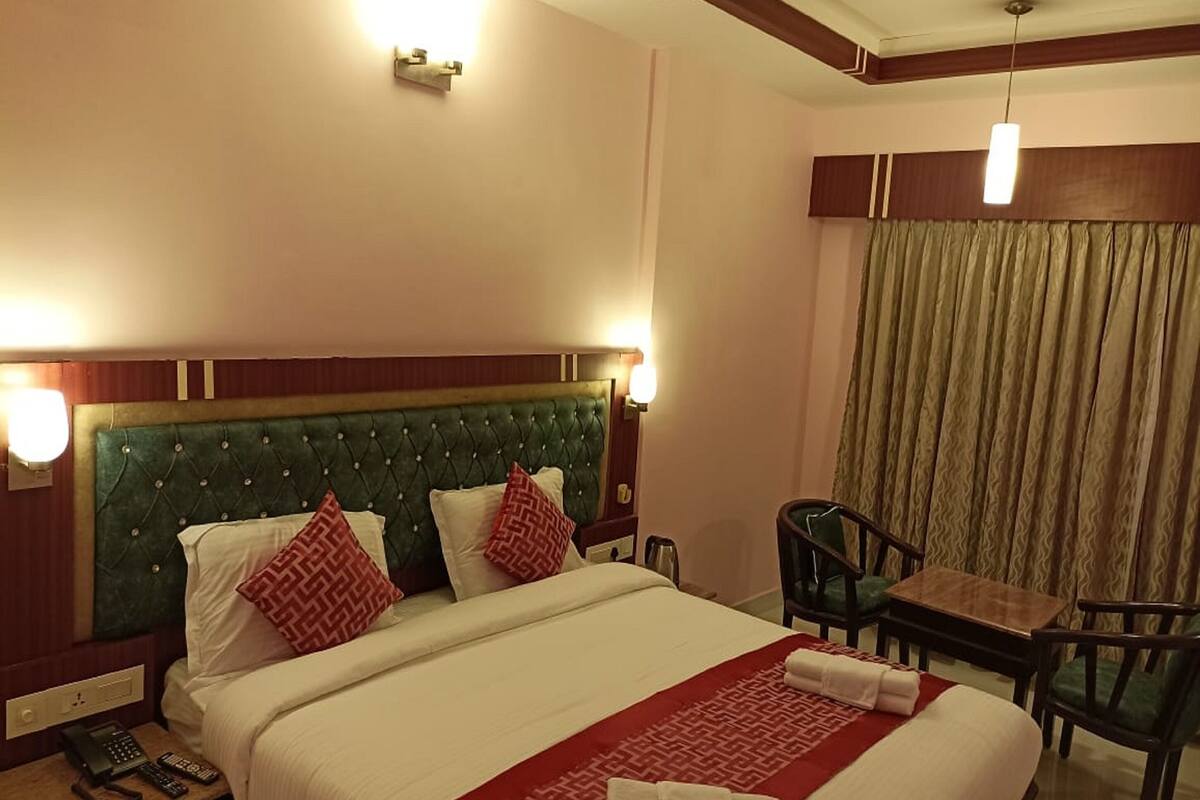 A hotel room with a bed, bedside tables, a desk, a chair, a ceiling fan, and a window with curtains.