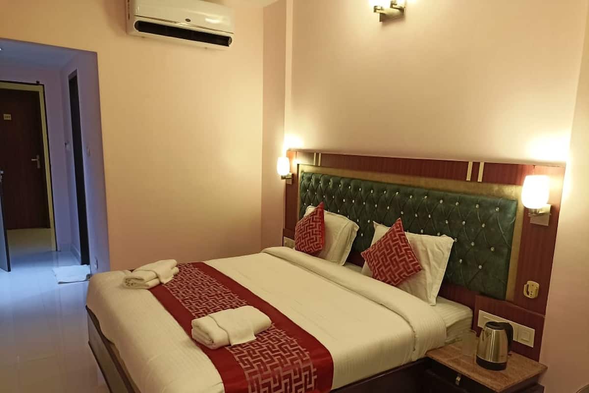 A hotel room with a large bed, a bedside table with a kettle, and a wall-mounted air conditioner.
