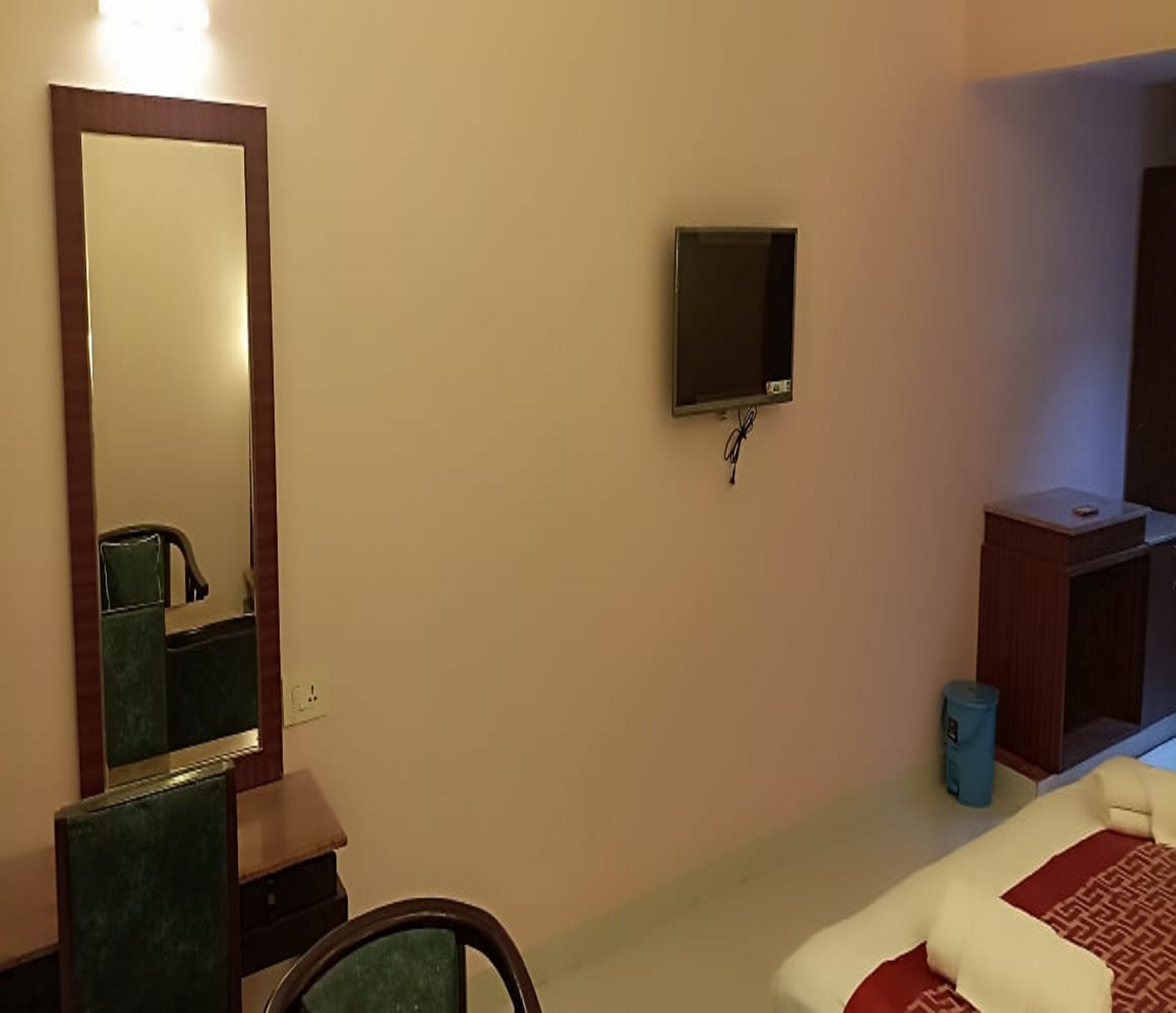 Habitación de hotel con un espejo grande, un televisor montado en la pared, un pequeño mueble de madera y una cama con colcha estampada.