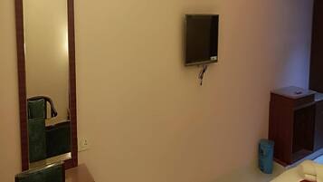 Habitación de hotel con un espejo grande, un televisor montado en la pared, un pequeño mueble de madera y una cama con colcha estampada.