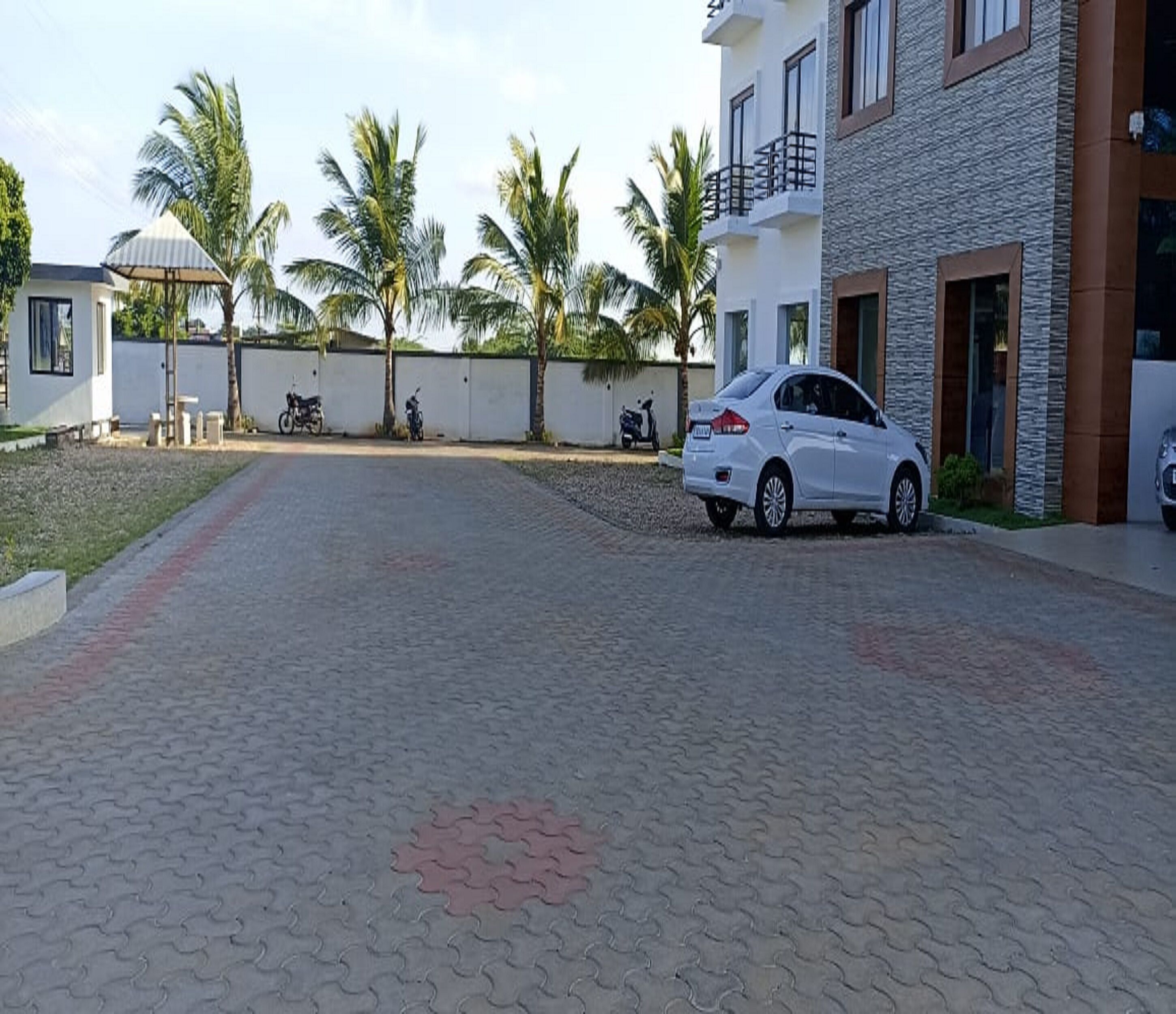 A paved driveway leading to a white car parked in front of a building with a stone facade and a balcony.