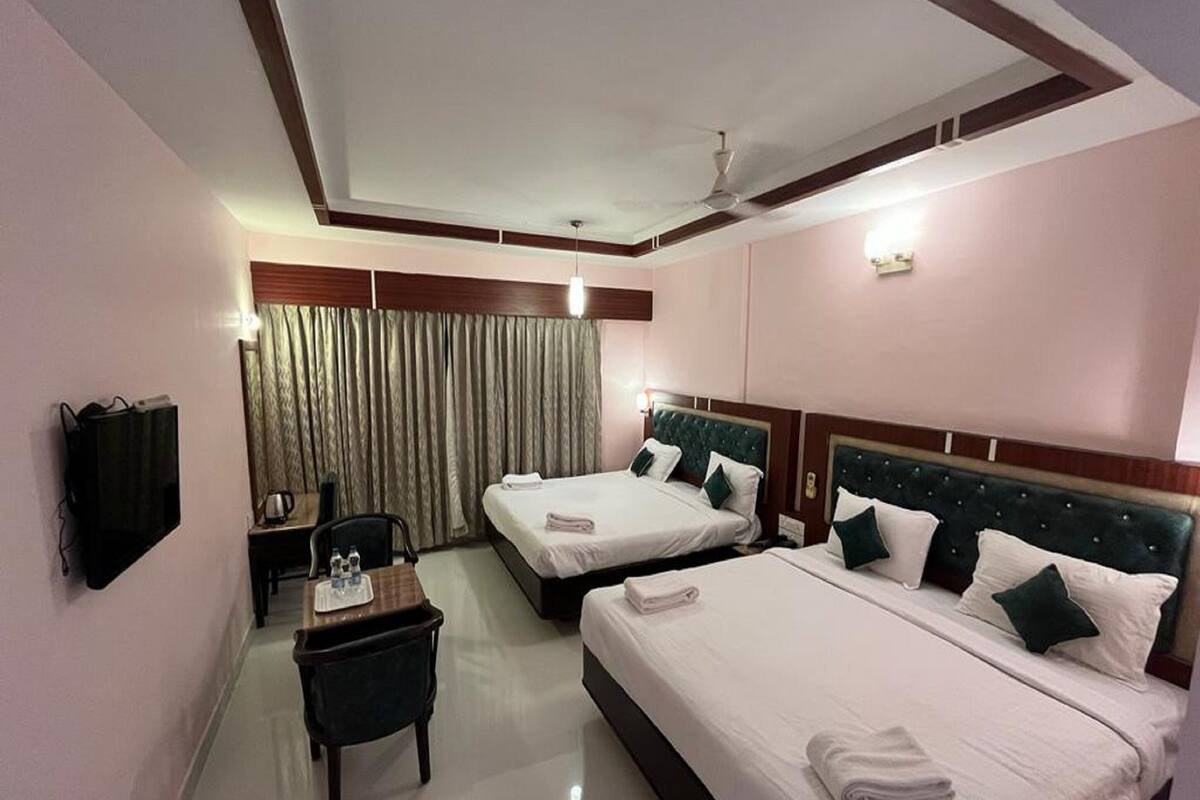 A hotel room with two beds, a desk, a chair, a TV, and a ceiling fan.