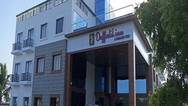 A modern hotel with a sign reading "Delffodil inn A pleasant stay". There are two cars parked in front and a person standing near the entrance. - Daffodil Inn (Kilvelur)