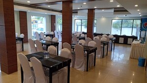 A spacious conference room with multiple tables and chairs, large windows, and a tiled floor. - Daffodil Inn (Kilvelur)