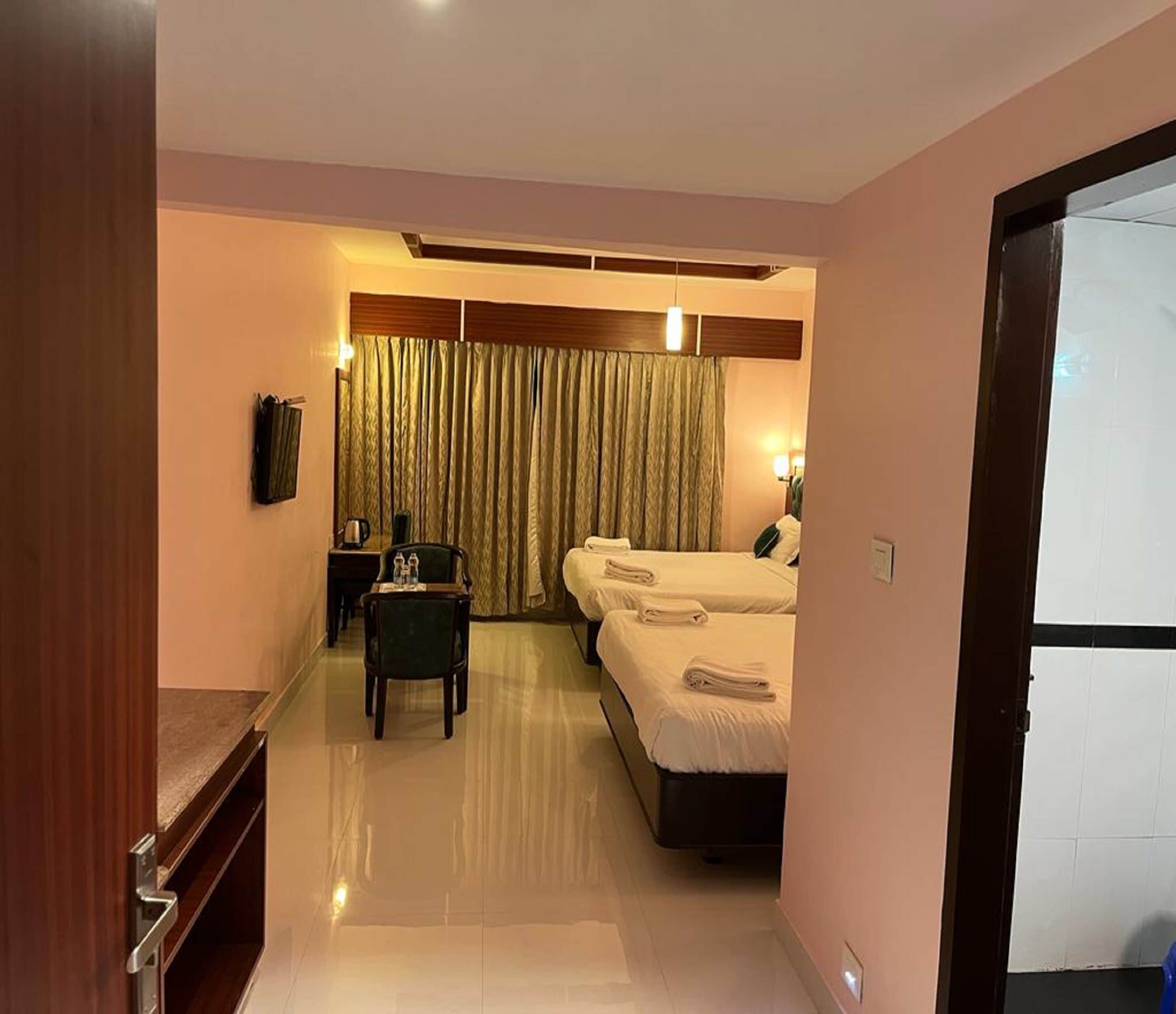 A hotel room with two beds, a desk, a chair, a flat-screen TV, and a large window with curtains.