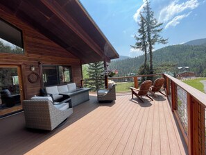 A wooden deck with outdoor seating, a view of a forested mountain range, and a building with large windows. - Amongst the Aspens in the Upper Valley (Red River)
