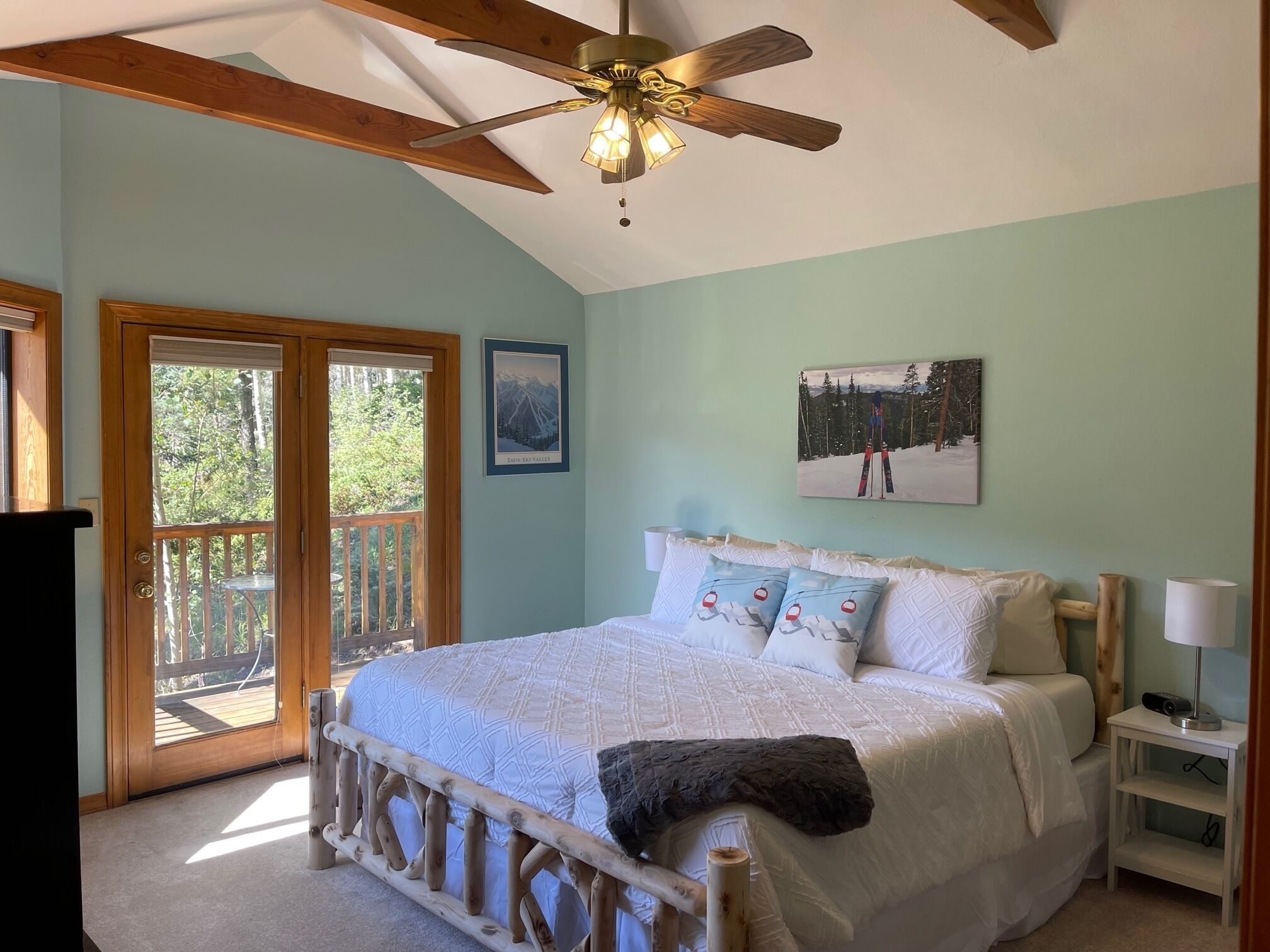A bedroom with a bed, a ceiling fan, a nightstand, and a view of a balcony.