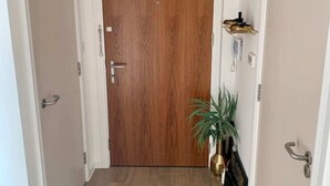 A hallway with a wooden door, a potted plant, and a radiator on the wall. - Stylish and Chic 1 Bedroom Apartment in Canning Town (London)
