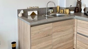 A modern kitchen with a grey countertop, wooden cabinets, and a sink. - Stylish and Chic 1 Bedroom Apartment in Canning Town (London)