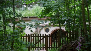 Un edificio rústico con una valla de madera, rodeado de abundante vegetación.