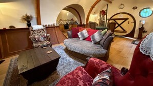 Una sala de estar acogedora con una mesa de centro de madera, un sillón estampado y un sofá rojo. Un arco de entrada da a una zona de cocina.