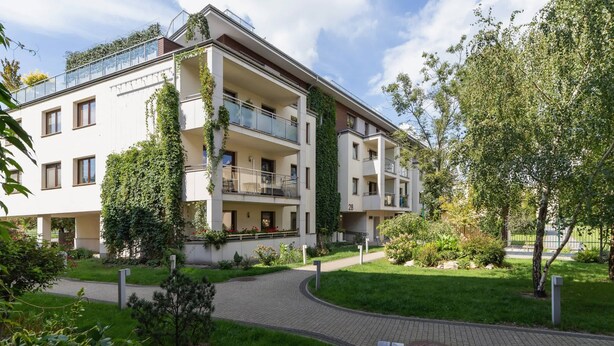 A multi-story residential building with balconies, a paved walkway, and surrounding greenery.