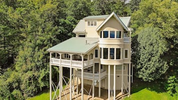 A multi-story house with a balcony and a wrap-around porch, surrounded by lush greenery.