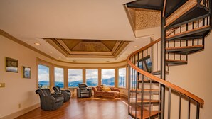 A spacious living room with a curved ceiling, a black spiral staircase, and large windows offering a mountain view.