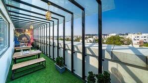 A rooftop terrace with glass walls, wooden tables, and potted plants. - Bangalore Times by Alaya Stays (Bengaluru)