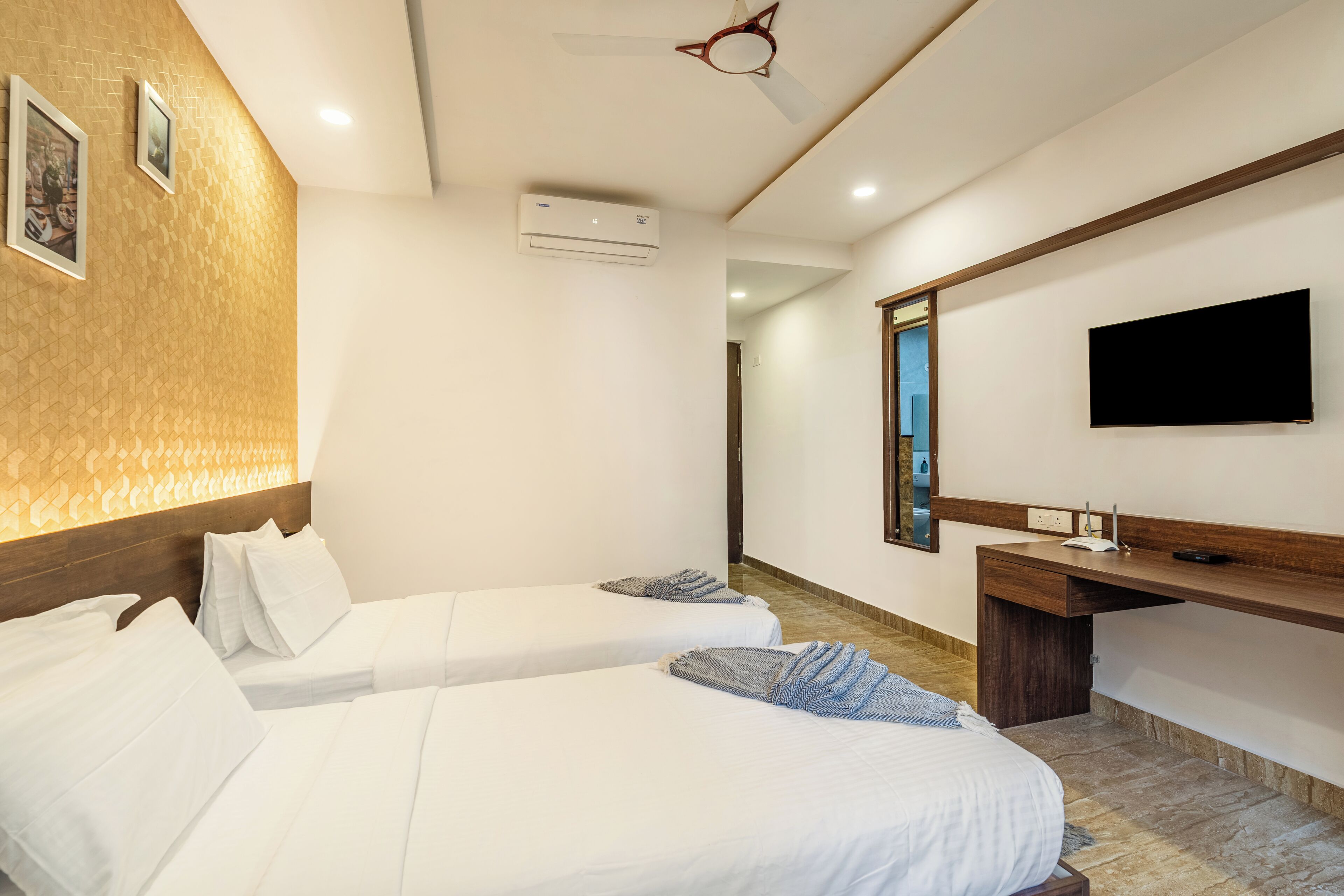 A hotel room with two beds, a desk, a flat-screen TV, and an air conditioning unit.