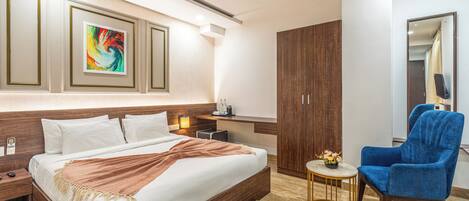 A modern hotel room with a large bed, a desk, a blue armchair, and a ceiling fan.