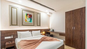 A modern hotel room with a large bed, a wooden wardrobe, a bedside table with a lamp, and a colorful abstract painting above the bed. - Bangalore Times by Alaya Stays (Bengaluru)