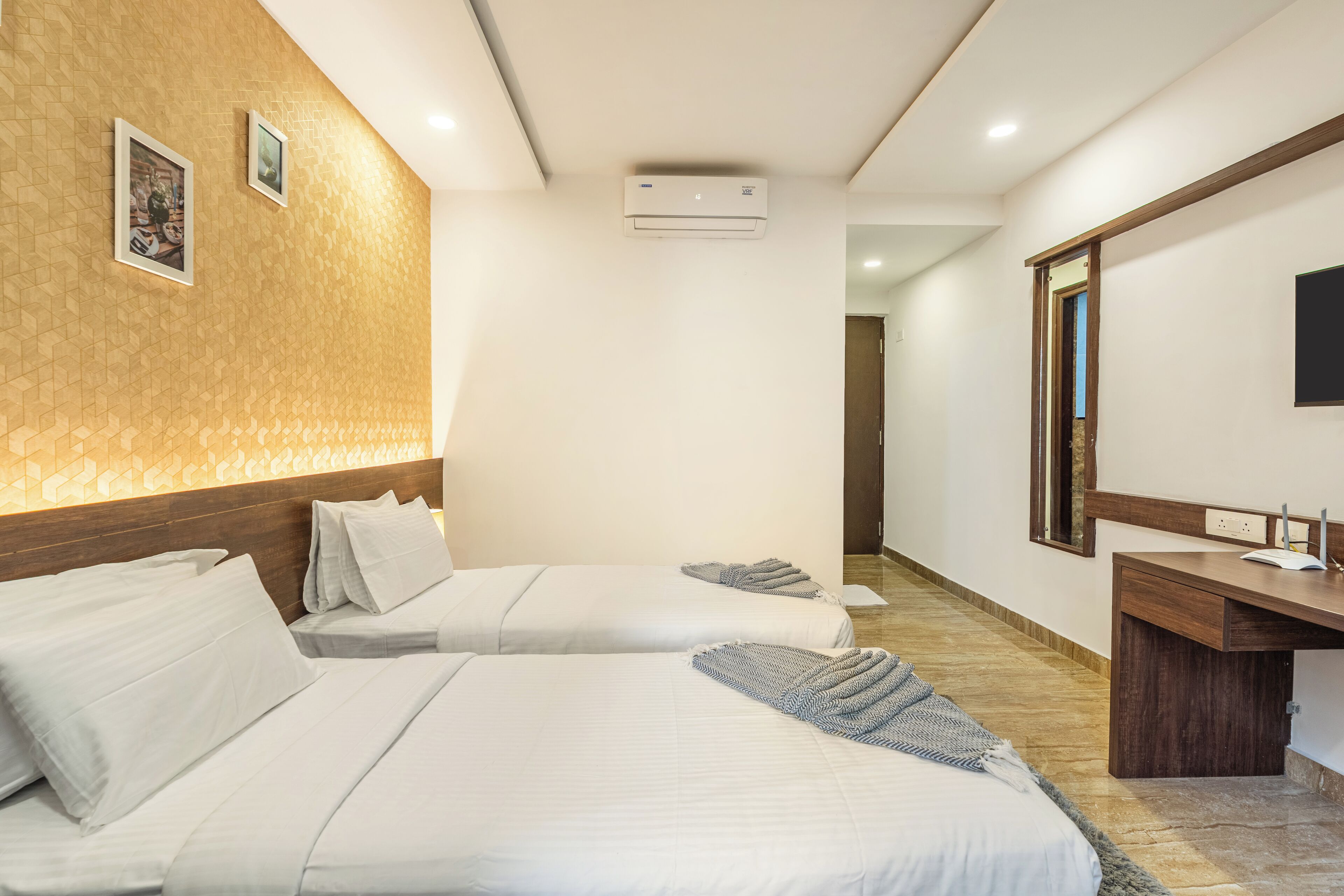 A hotel room with two beds, a wooden headboard, a desk with a mirror, and a wall-mounted air conditioner.