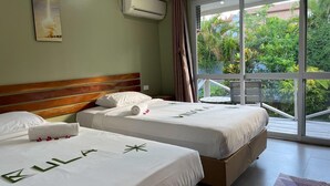 A hotel room with two beds, a large window with a view of greenery, an air conditioning unit, and a ceiling light.