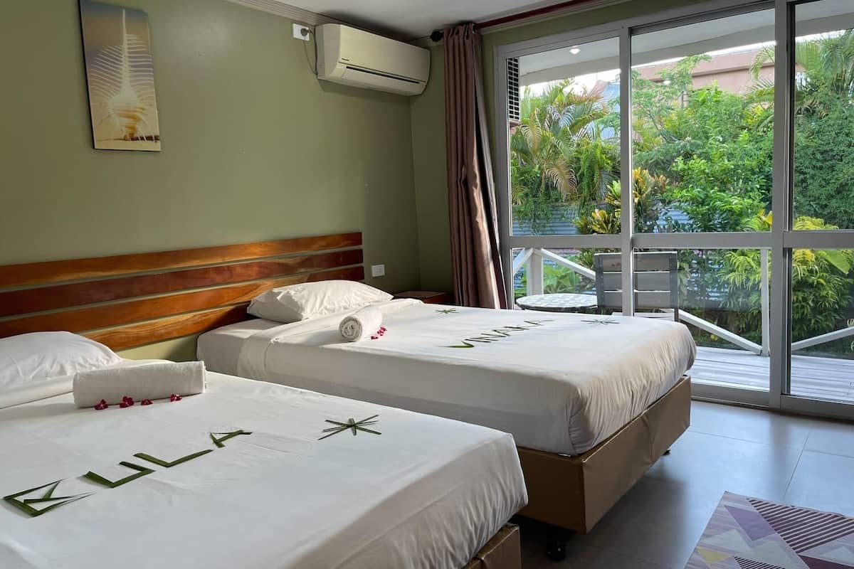 A hotel room with two beds, a large window with a view of greenery, an air conditioning unit, and a ceiling light.