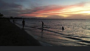 A beach scene with people walking along the shore during sunset.