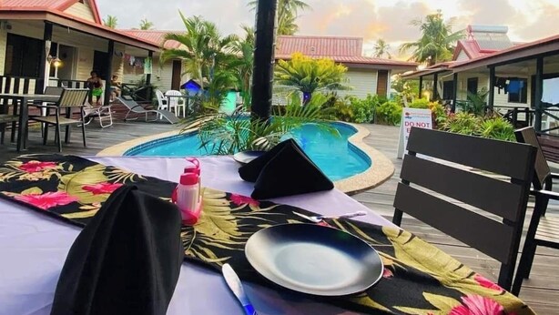 A poolside dining area with a table set for two, a pool, and a view of the surrounding buildings and palm trees.
