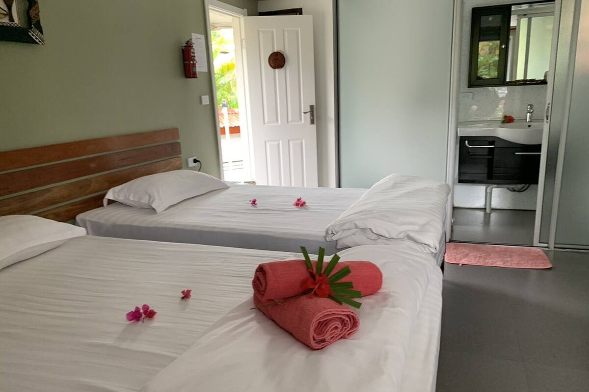 A hotel room with two beds, a bathroom with a sink and mirror, and a door leading to a balcony.