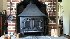 Una chimenea de ladrillo con un horno negro, un suelo de madera con patrón de espiga y un perchero colgado.