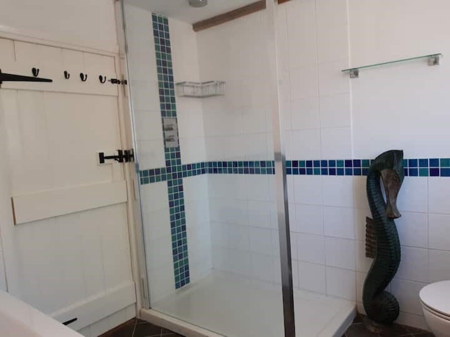 Een badkamer met een douchecabine van glas, witte betegelde wanden en een groene decoratieve slangbeeldhouwkunst.