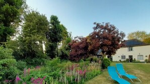 Un jardín con césped, una silla azul y un edificio blanco al fondo.