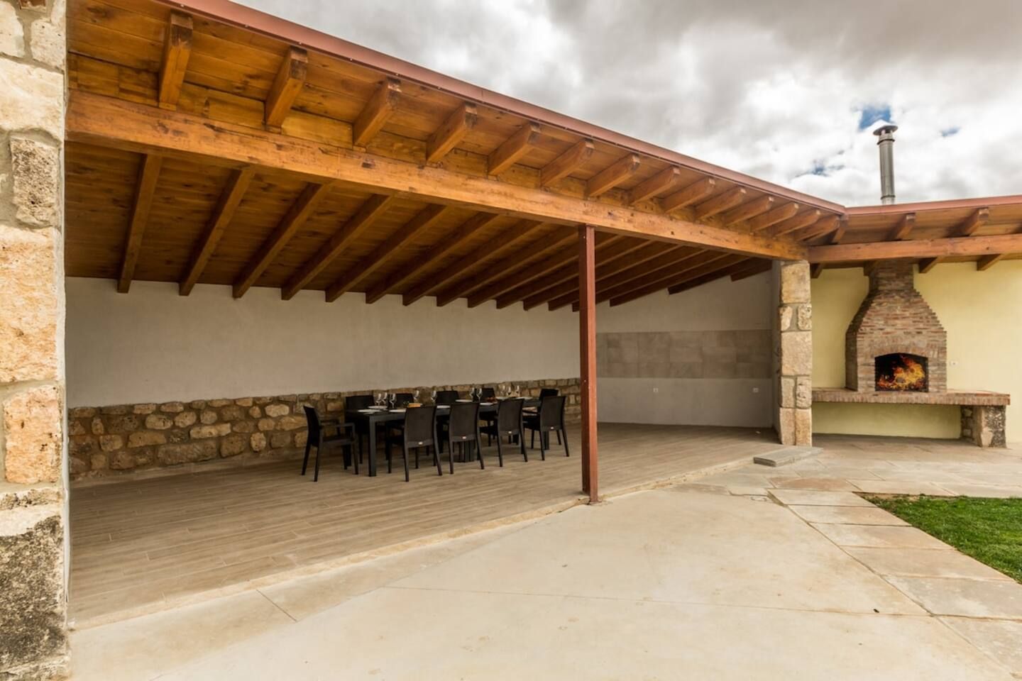 An outdoor patio with a stone wall, wooden ceiling, and a brick fireplace.