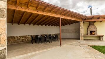 An outdoor patio with a stone wall, wooden ceiling, and a brick fireplace.