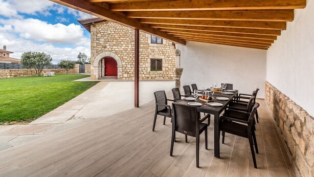 An outdoor patio with a stone wall, a wooden pergola, and a dining table set for six. - Fidalsa Rest Station (Villadiego)