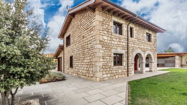A stone building with a flat roof, a paved entrance, and a grassy area. - Fidalsa Rest Station (Villadiego)