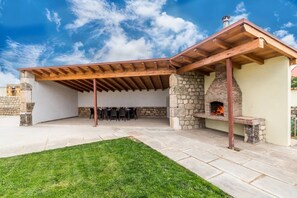 An outdoor patio with a stone fireplace, wooden pergola, and a grassy area.