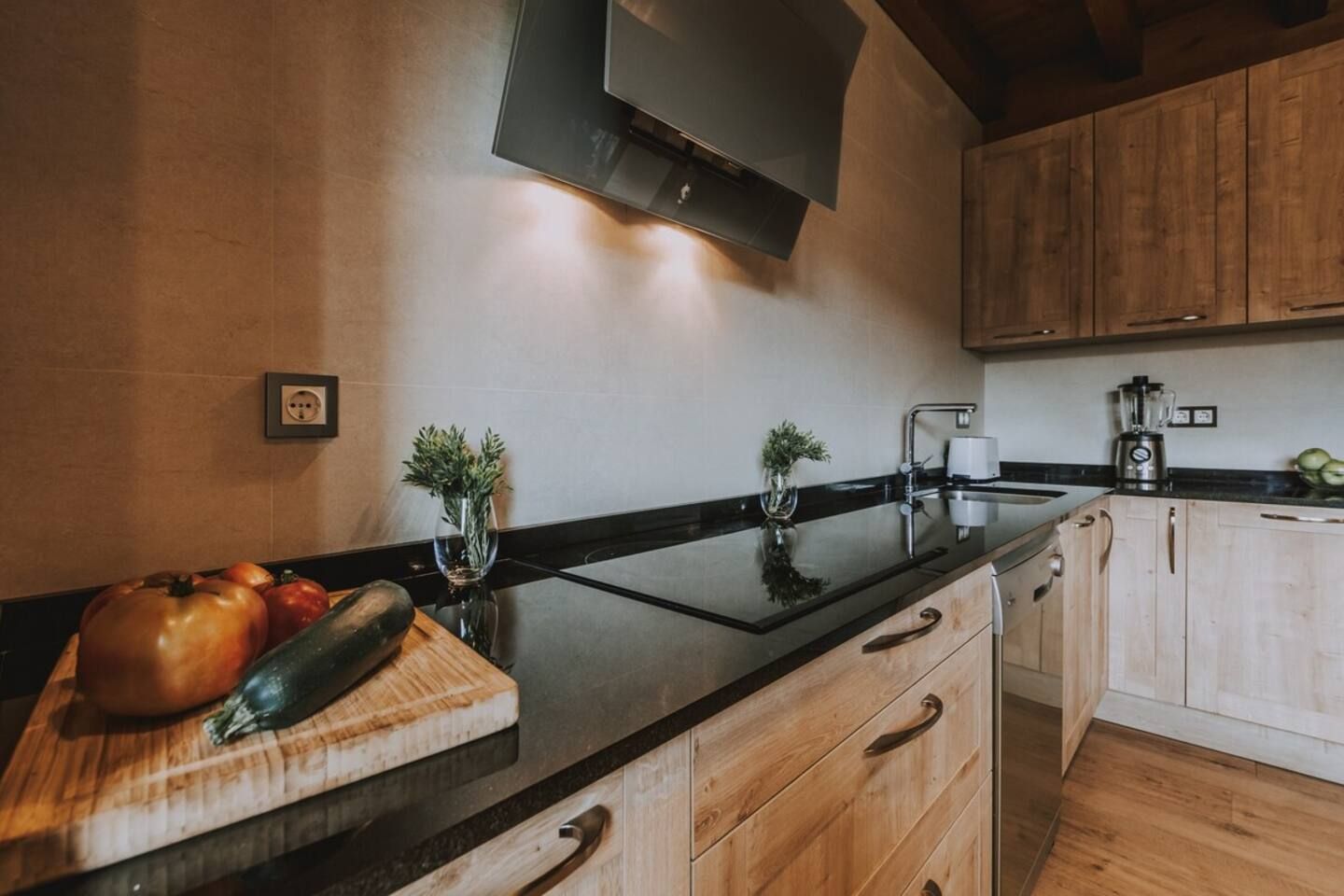 Una cocina moderna con armarios de madera, encimera negra y tabla de cortar con verduras.