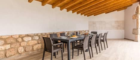 A dining area with a stone wall, wooden ceiling beams, and a tiled floor.
