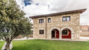 A stone building with a red door and arched windows, surrounded by a well-maintained lawn. - Fidalsa Rest Station (Villadiego)