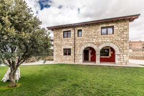 A stone building with a red door and arched windows, surrounded by a well-maintained lawn.
