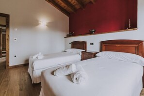 A hotel room with two beds, wooden headboards, a red accent wall, and a wooden floor.