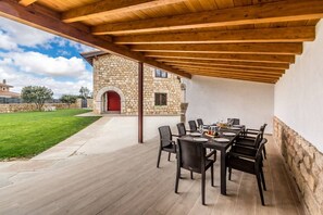 Um pátio externo com um edifício de pedra, uma porta vermelha e uma mesa posta para refeições.