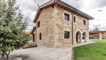 Un edificio de piedra con techo plano, entrada empavedada y un área verde al frente.