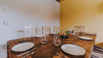 Una mesa de comedor dispuesta con platos, cubiertos y vasos, con un frutero sobre la mesa.