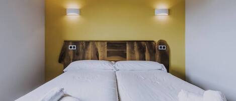 A double bed with white linens and two wall-mounted light fixtures.