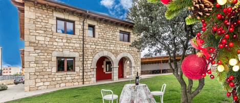 A stone building with a red door, a table with chairs, and Christmas decorations.