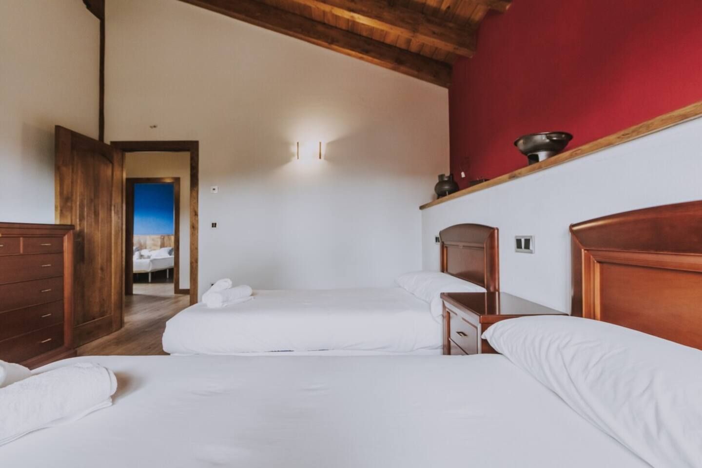 Habitación de hotel con dos camas, cabeceros de madera, una pared de acento roja y vistas a un balcón.
