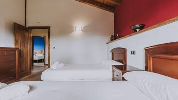 Habitación de hotel con dos camas, cabeceros de madera, una pared de acento roja y vistas a un balcón.