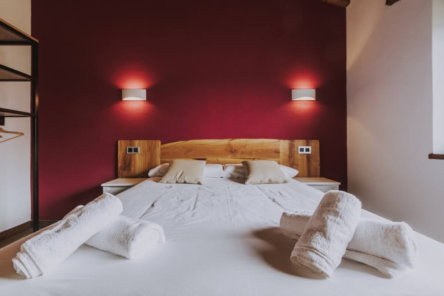 Habitación de hotel con cabecera de madera, dos mesitas de noche y dos lámparas fijadas a la pared.