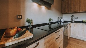 A modern kitchen with a black countertop, wooden cabinets, a built-in oven, and a wall-mounted TV. - Fidalsa Rest Station (Villadiego)